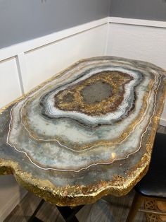 the table is made out of agate and gold leafy material, with a black leather chair underneath it