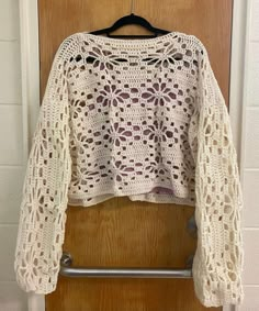 a white crocheted sweater hanging on a wooden door with a hanger in front of it