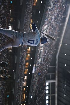 a baseball player is in mid air with his bat raised above the crowd at a stadium