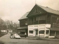 an old black and white photo of a man standing in front of a building with a car parked on the street