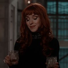 a woman with red hair holding a glass in her right hand and looking at the camera