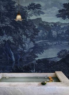 a bathtub in front of a wall with a painting on it and lights hanging from the ceiling