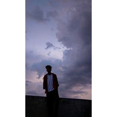 a man standing on top of a cement wall under a cloudy sky with clouds in the background