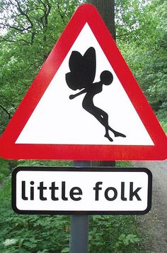 a little folk sign on a pole in front of some trees and dirt road signs