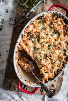 a casserole dish with meat and cheese in it on a wooden table next to utensils