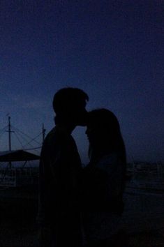 a man and woman standing next to each other in front of a boat at night