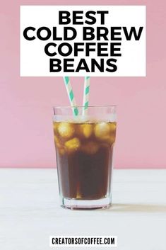 a glass filled with liquid and two straws on top of it next to a sign that says best cold brew coffee beans