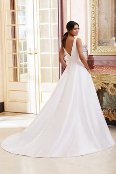 a woman in a white wedding dress is standing near a mirror and looking at the floor