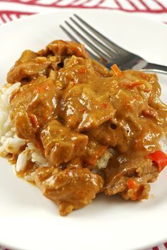 a white plate topped with meat covered in gravy and rice next to a fork