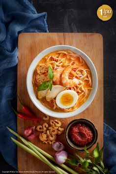 a bowl of noodles with shrimp, eggs and vegetables on a cutting board next to some seasonings