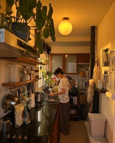 a woman standing in a kitchen preparing food on top of a wooden counter next to a potted plant