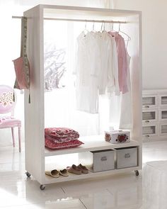 a white closet with clothes hanging on the rack and shoes sitting on the floor next to it