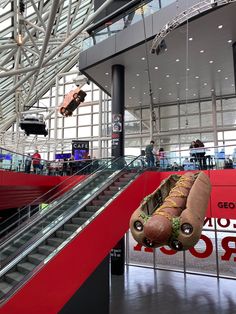 a giant hot dog hanging from the side of an escalator in a building