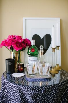 a table topped with bottles and glasses next to a vase filled with flowers on top of a table