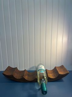 a wooden boat shaped bottle holder on a blue counter top with a white wall behind it