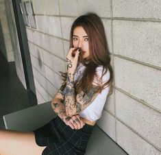 a woman with tattoos sitting on a bench next to a wall and holding her hand up to her mouth