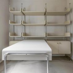 a white bed sitting in the middle of a room next to a wall mounted shelving unit