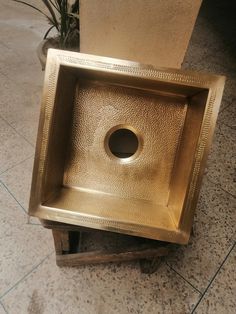 a square metal sink sitting on top of a wooden stand next to a potted plant