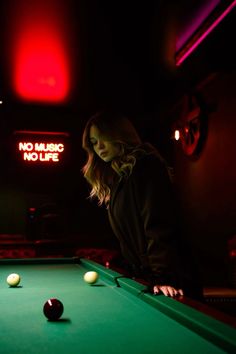 a woman leaning over a pool table in a dark room with neon lights behind her