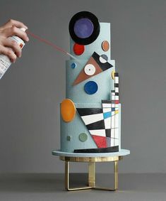 a person is painting the top of a multi - colored cake