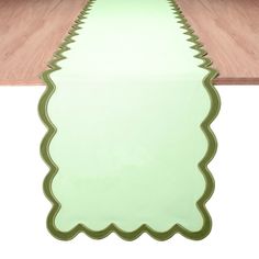 a green table runner with scalloped edges on a wood floor in front of a white wall