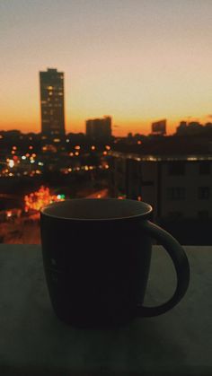 a black coffee cup sitting on top of a table next to a cityscape