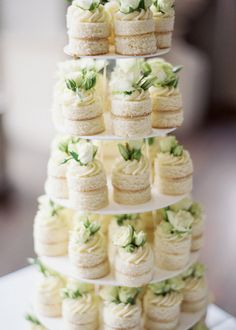 a three tiered cake with white flowers on the top and green leaves on the bottom