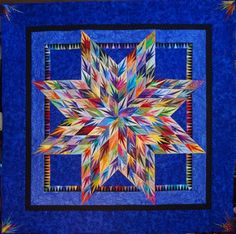 a blue quilt with a multicolored star on the front and center piece in the middle