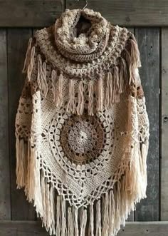 a crocheted shawl hanging on a wooden wall with fringes and beads