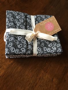 a stack of black and white wrapping paper with a pink tag tied to it on top of a wooden table