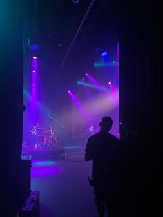 a man standing in front of a stage with purple and green lights on it's sides