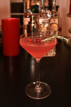 a red drink sitting on top of a black table next to bottles and candle holders