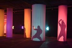 a person standing in front of three tall pillars with colored lights on the walls behind them