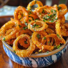 some onion rings are in a blue and white bowl on a wooden table with parsley