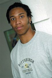 a young man with dreadlocks standing in front of a white wall and looking at the camera