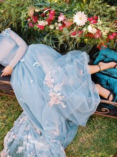 a woman in a blue dress is laying on the ground next to flowers and plants