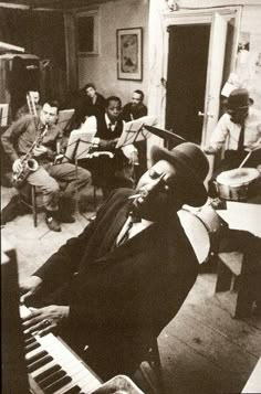 an old photo of a man playing the piano in a room with other people around him