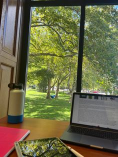 an open laptop computer sitting on top of a wooden desk next to a large window