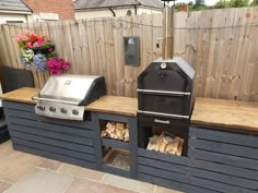 an outdoor bbq grill with wood logs on the counter and flowers in pots behind it