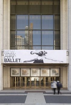 a large advertisement on the side of a building for new york ballet company, with people walking by