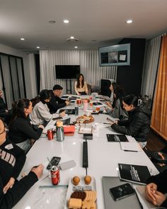 a group of people sitting at a long table with laptops and food on it