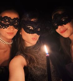 three women in masquerades pose for a photo while holding a lit candle