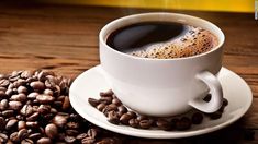 a cup of coffee sitting on top of a white saucer next to roasted coffee beans