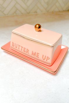 a pink butter me up container sitting on top of a white counter next to a gold plate