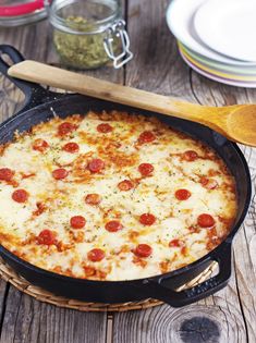 a pizza sitting in a pan on top of a wooden table next to plates and utensils