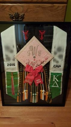 a graduation cap and tassels are on display in a shadow box with ribbon