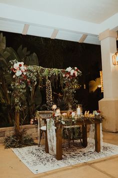 a table set up with flowers and greenery for a wedding reception in the evening