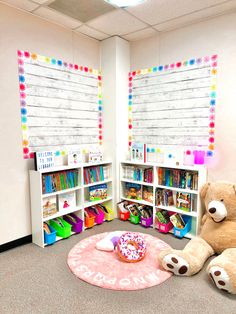 a teddy bear sitting on the floor next to a bookcase with two large stuffed animals