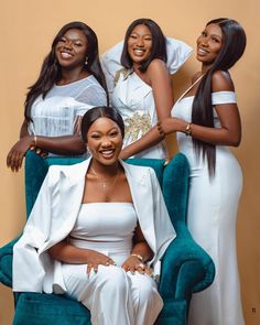 three women in white dresses sitting on a blue chair and posing for the camera with their arms around each other