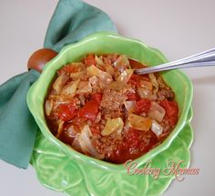 a green bowl filled with pasta and meat on top of a green napkin next to a wooden spoon